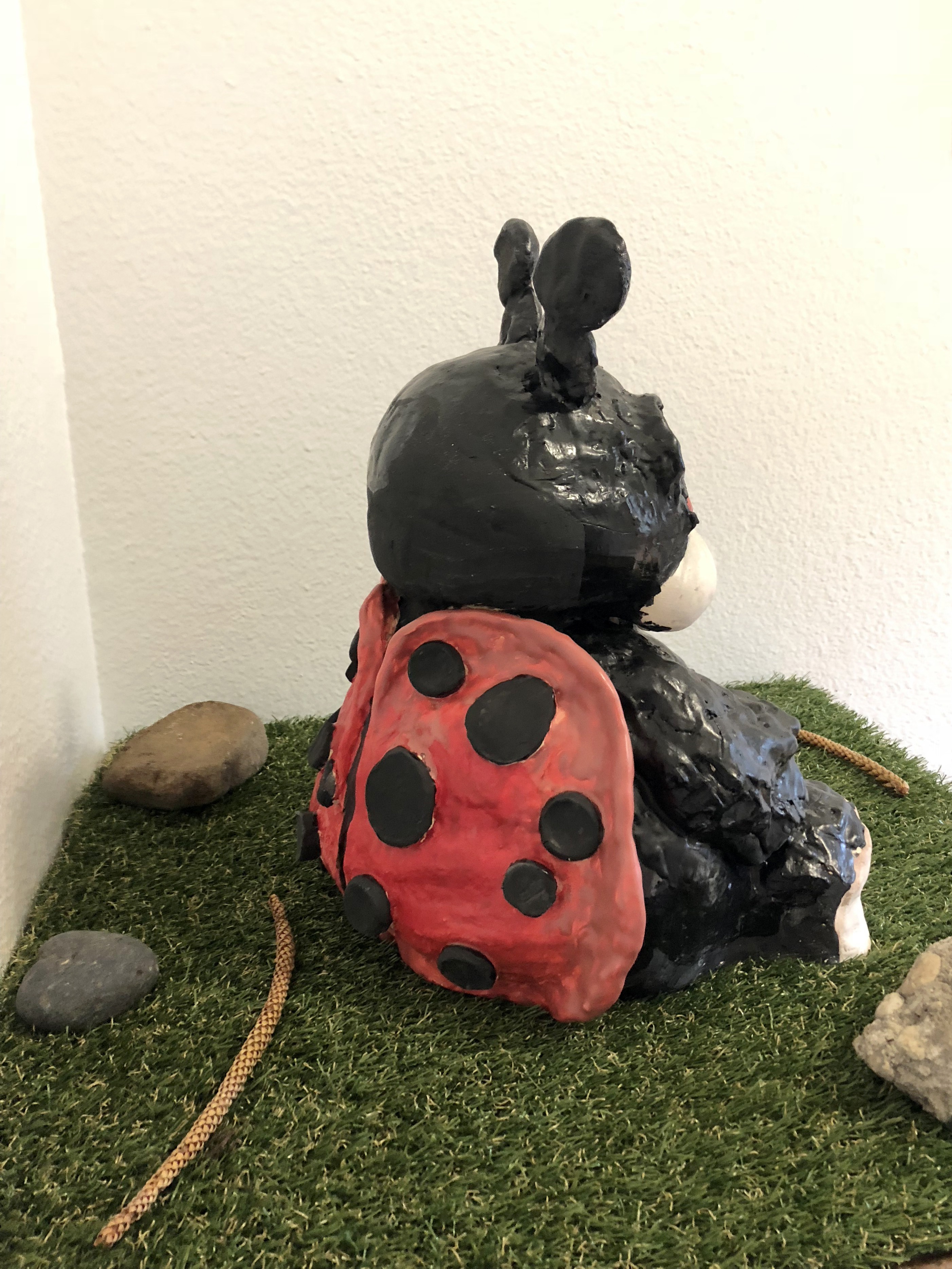 side view detail of a ceramic sculpture of a black ladybugy on a small table covered in astroturf